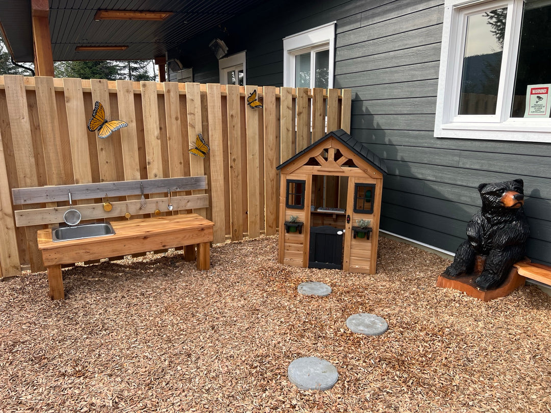 Timber playhouse, workbench and bear carving in an outdoor play corner